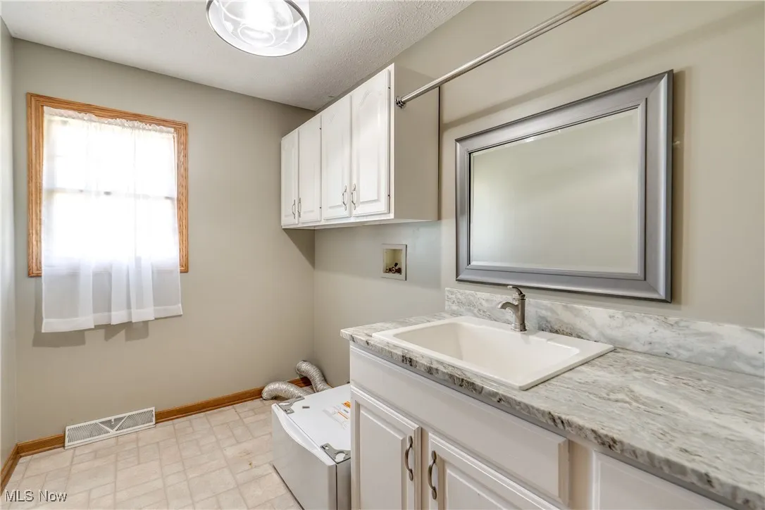 Main level laundry with washer hookup, cabinet space, and a textured ceiling
