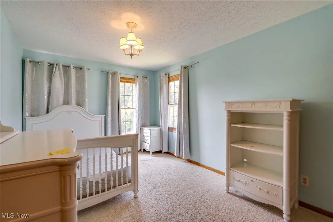 Bedroom with light colored carpet, a crib, a textured ceiling, and a chandelier