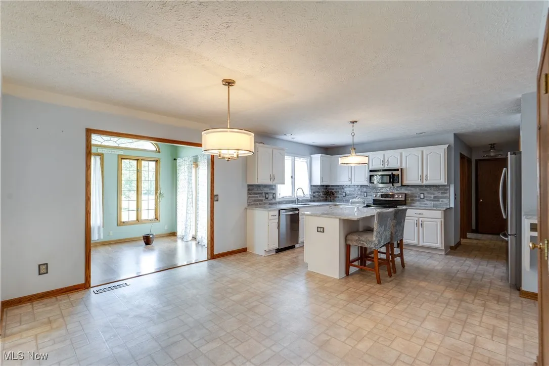 Kitchen featuring a kitchen bar, a kitchen island, backsplash, white cabinetry, and a textured ceiling