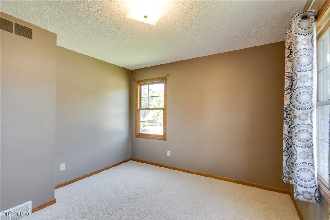 Carpeted empty room with a textured ceiling and baseboards