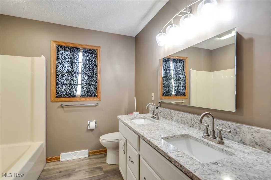Bathroom featuring a textured ceiling, light wood-type flooring, double vanity, and bathing tub / shower combination