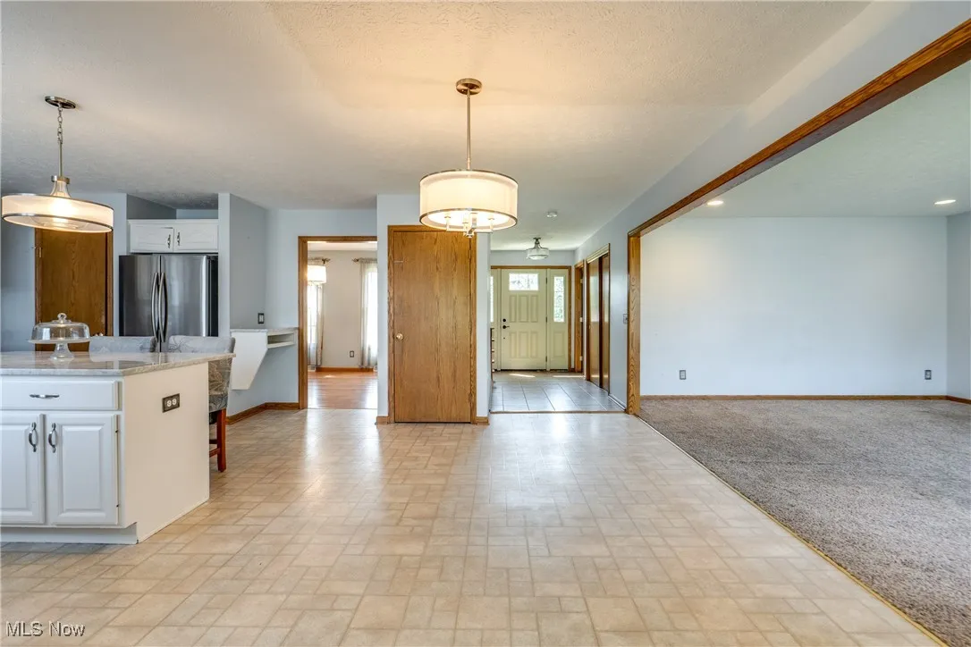 Kitchen featuring white cabinetry, open floor plan, freestanding refrigerator, light stone countertops, and a textured ceiling
