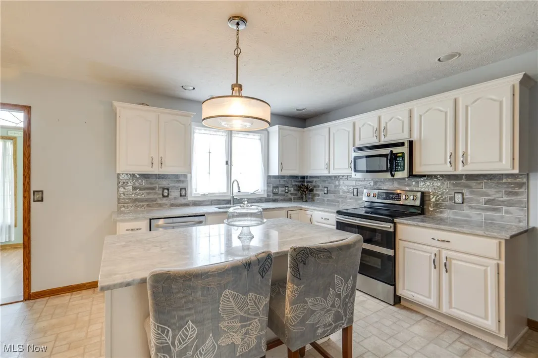 Kitchen with tasteful backsplash, appliances with stainless steel finishes, pendant lighting, a kitchen island, and a kitchen bar