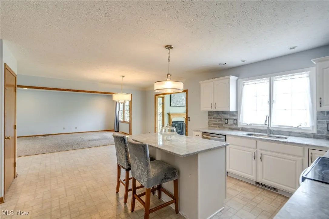 Kitchen featuring a breakfast bar area, white cabinetry, a center island, decorative light fixtures, and tasteful backsplash