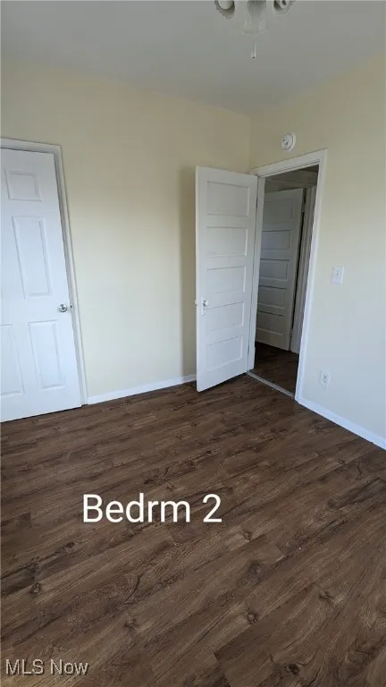 Unfurnished bedroom featuring dark wood-type flooring and baseboards
