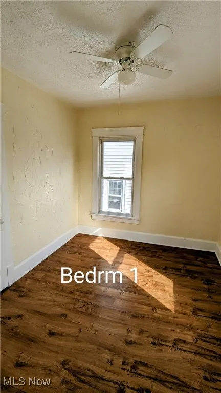 Empty room featuring a textured ceiling, a textured wall, and dark wood-style flooring