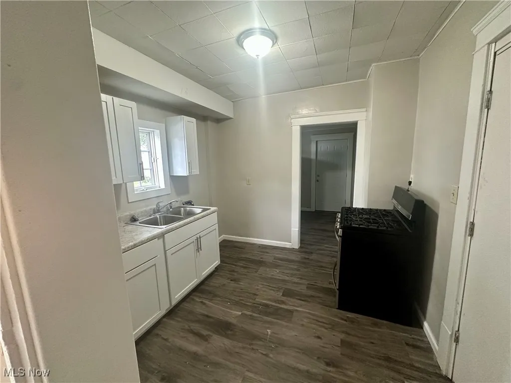 Kitchen featuring stainless steel range with gas stovetop, light countertops, dark wood-style floors, and white cabinets