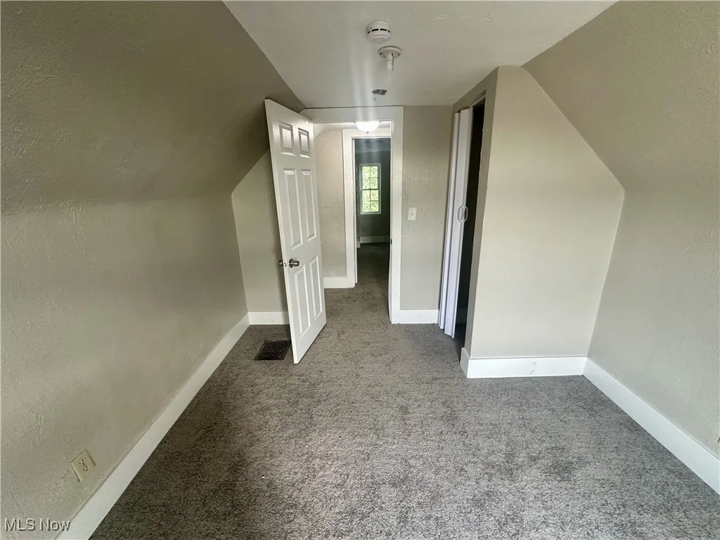 Additional living space with light carpet, lofted ceiling, and a textured wall