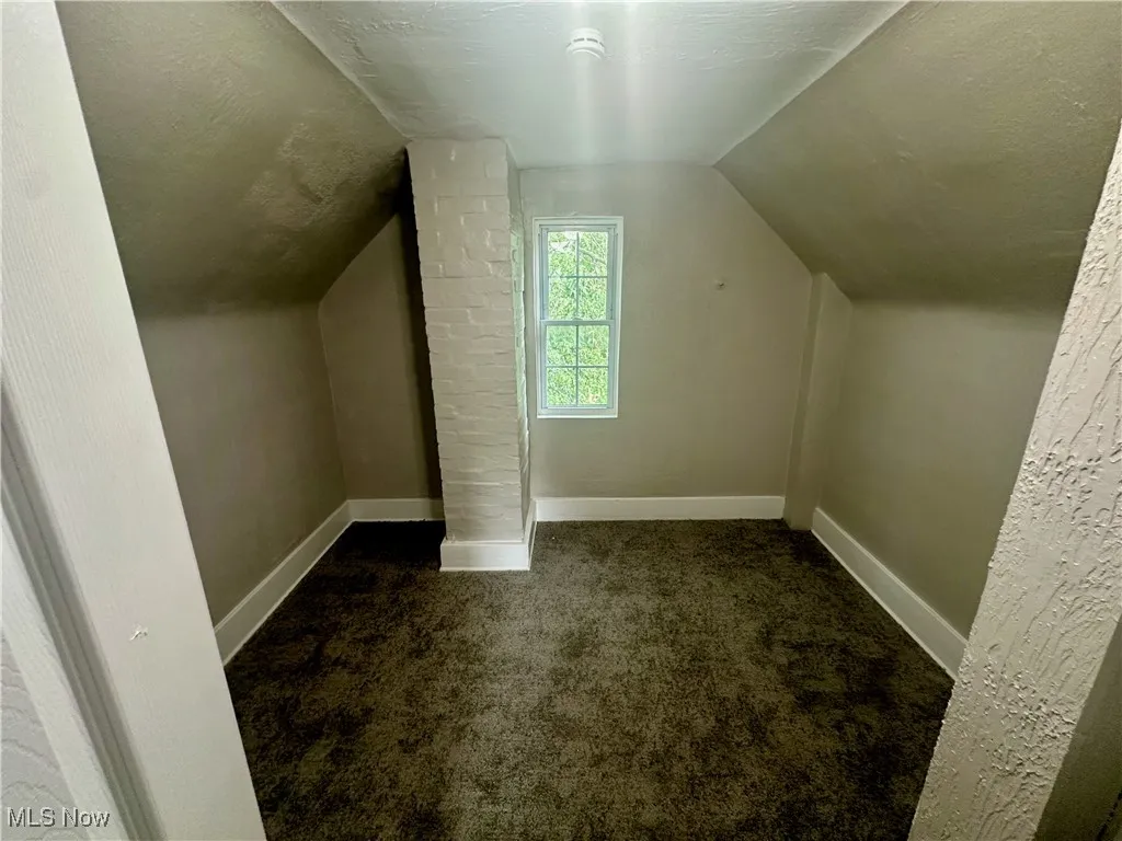 Bonus room featuring a textured ceiling, dark carpet, and vaulted ceiling
