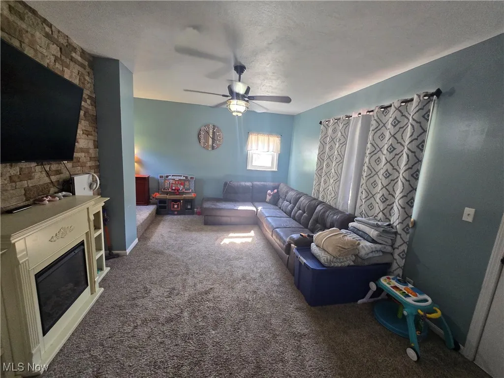 Living room featuring carpet, a fireplace, a textured ceiling, and ceiling fan