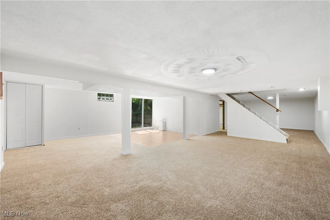 Below grade area featuring light carpet, a textured ceiling, and stairway