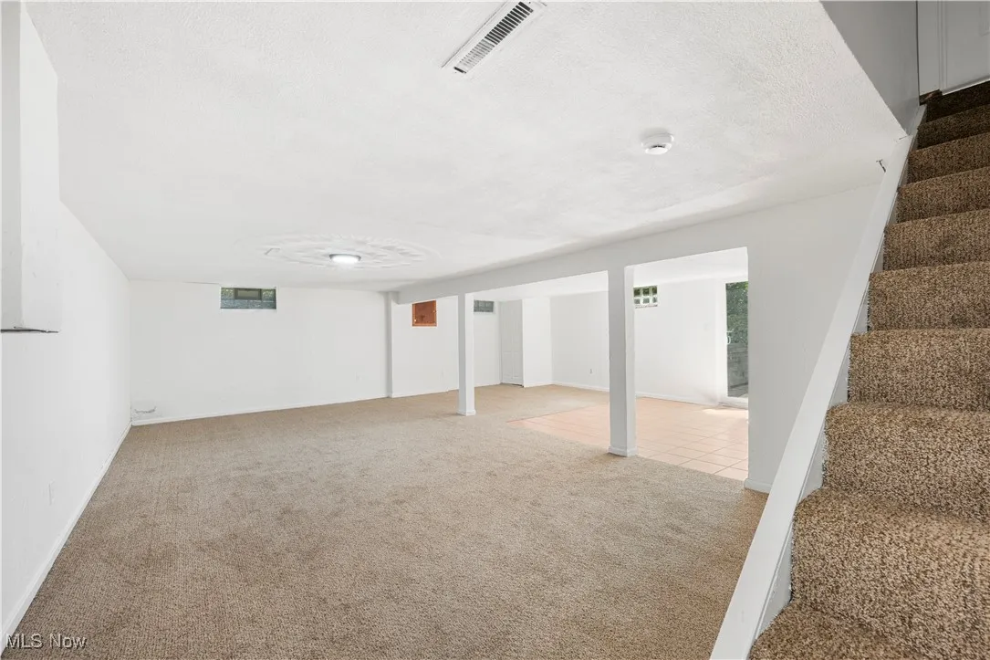 Basement featuring light carpet, stairway, and a textured ceiling