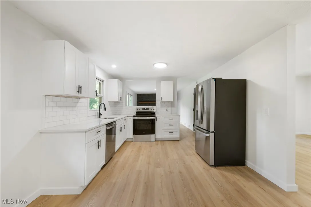 Kitchen featuring white cabinets, appliances with stainless steel finishes, light wood finished floors, tasteful backsplash, and recessed lighting