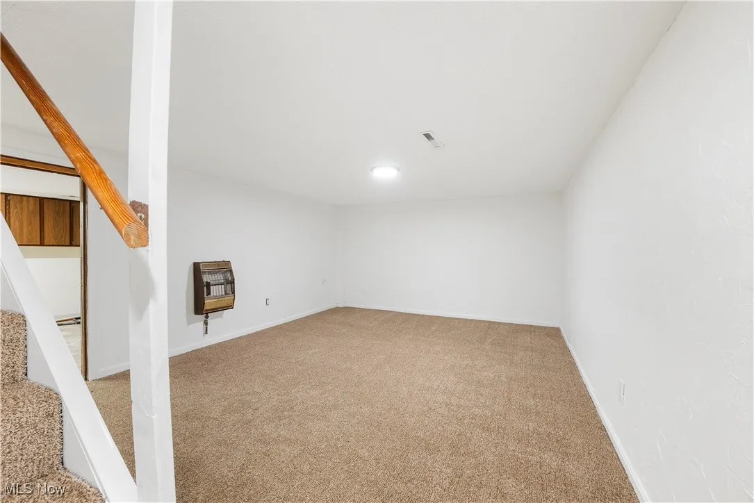 Finished basement with light carpet, heating unit, and stairs