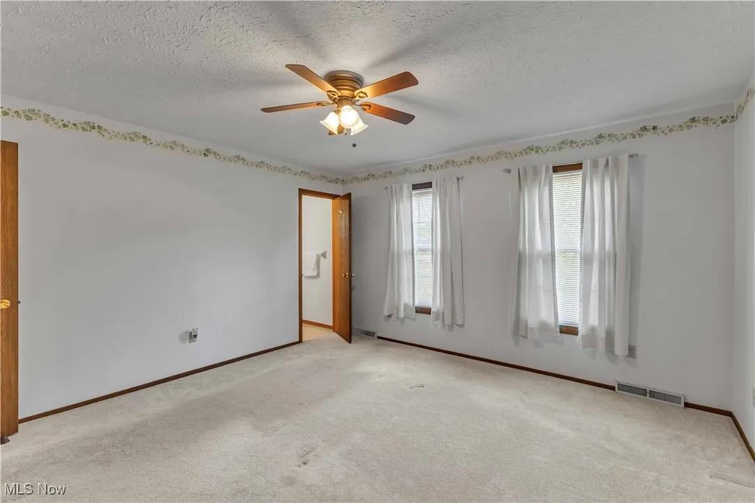 Spacious primary bedroom featuring light colored carpeting, neutral wall color, overhead ceiling fan and 2 windows.