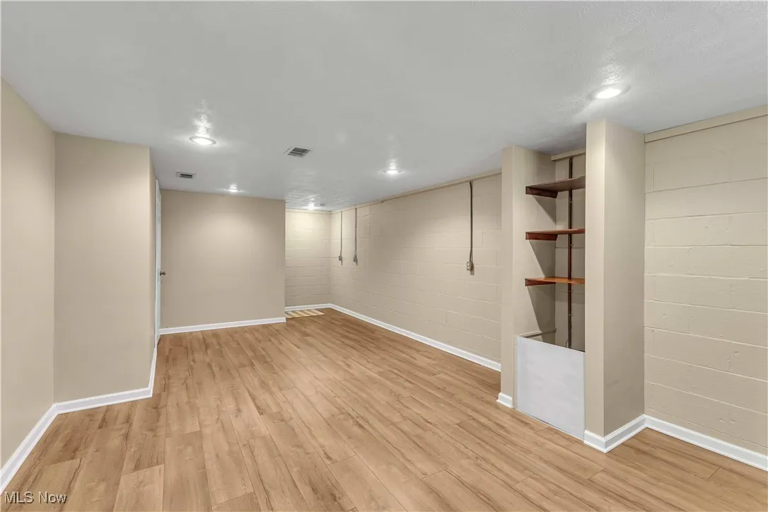 Finished living space in the basement featuring light colored flooring, neutral painted walls, glass block windows and recessed lighting.