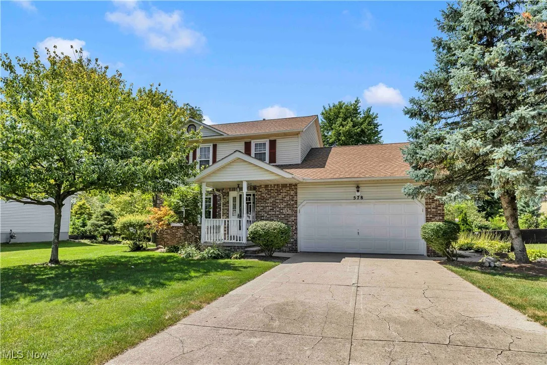 Traditional colonial home with an attached 2 car garage, manicured front lawn, concrete driveway, and covered front porch