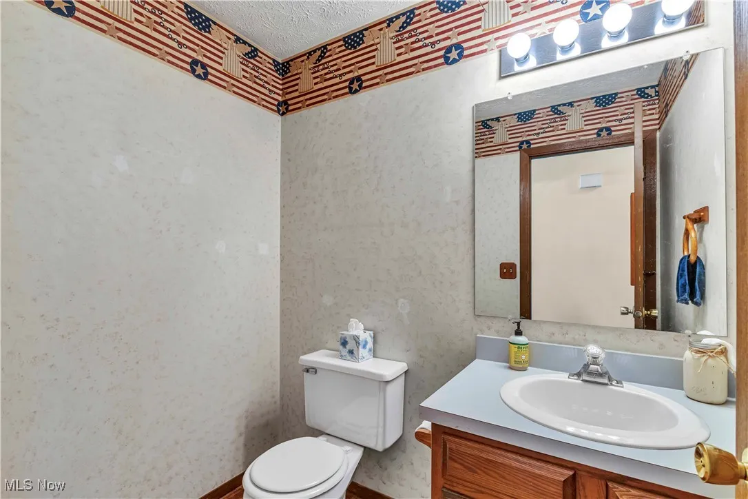 Half bathroom located on the main floor with toilet, wood vanity and mirror above.