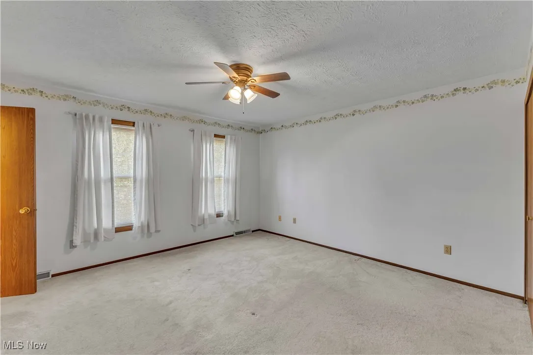 Spacious primary bedroom featuring light colored carpeting, neutral wall color, overhead ceiling fan and 2 windows.
