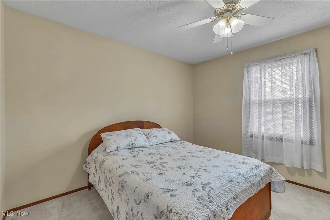Bedroom with light colored carpeting, window and ceiling fan.