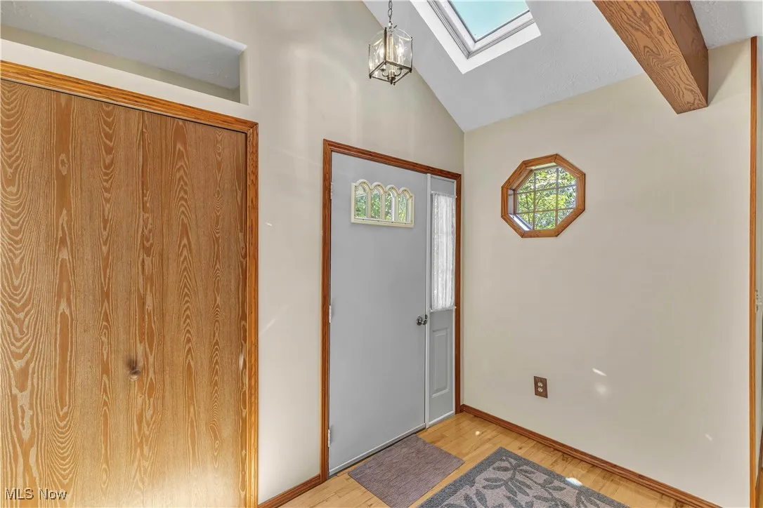 Foyer entrance featuring a skylight, port hole window, coat closet, light wood-style flooring, and a chandelier