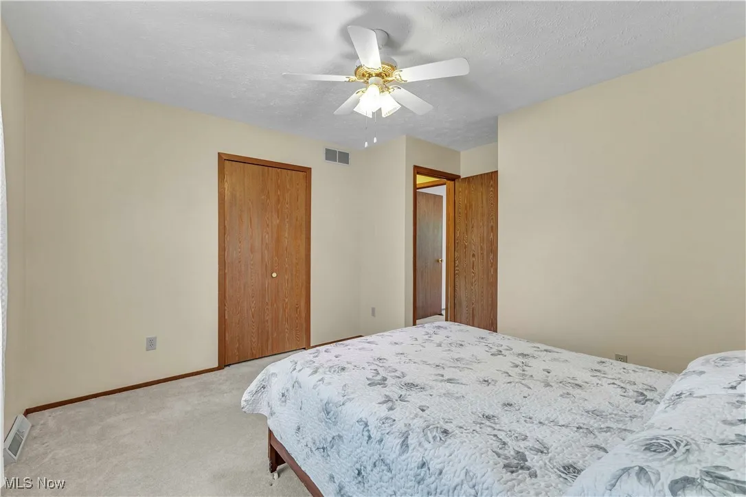 Bedroom with light colored carpeting, closet and ceiling fan.
