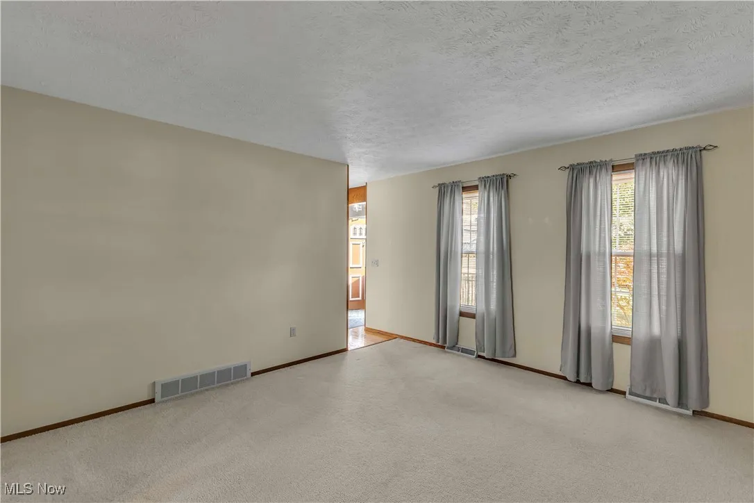 Living room at the front of the home off foyer featuring light carpeting and neutral color walls and two windows.