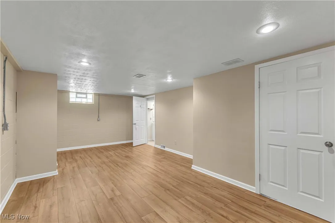 Finished living space in the basement featuring light colored flooring, neutral painted walls, glass block windows and recessed lighting.
