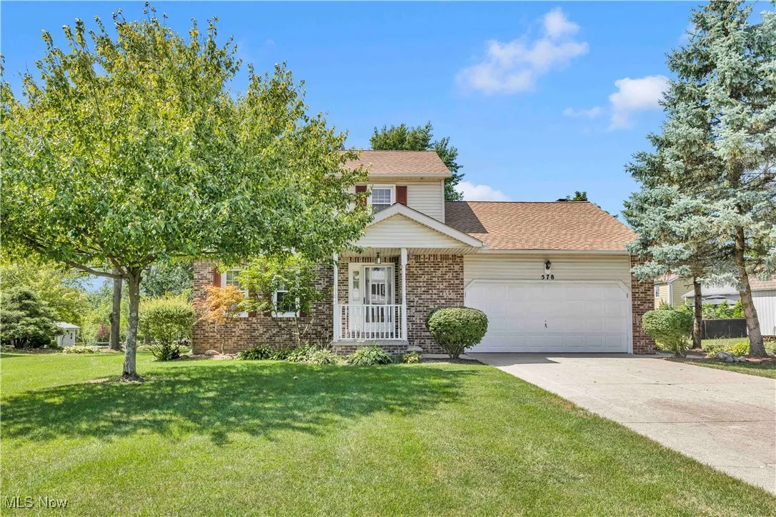 Traditional colonial home with an attached 2 car garage, manicured front lawn, concrete driveway, and covered front porch
