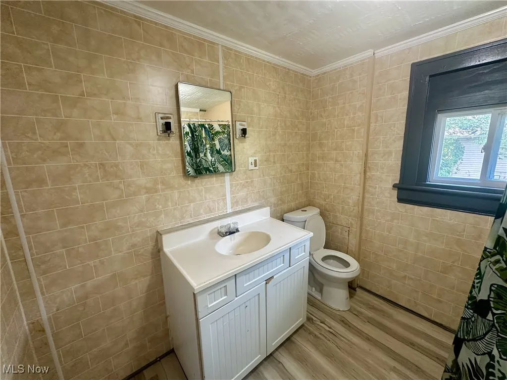 Bathroom featuring light wood-style flooring, vanity, tile walls, ornamental molding, and curtained shower