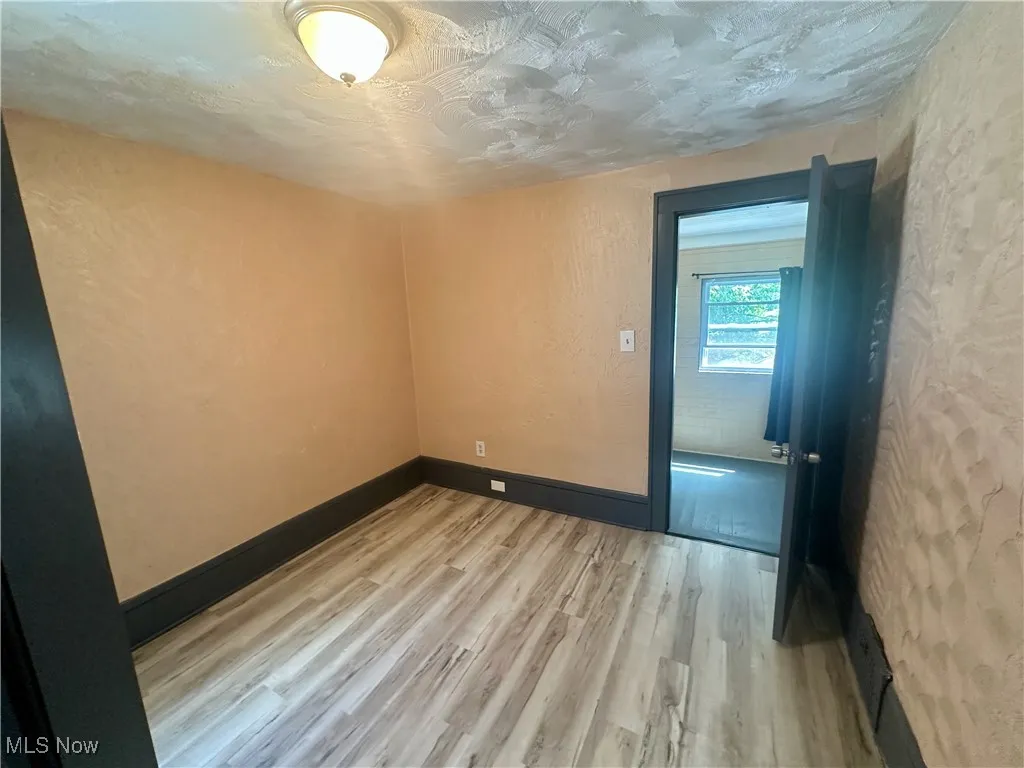 Unfurnished room featuring light wood finished floors, a textured wall, and a textured ceiling