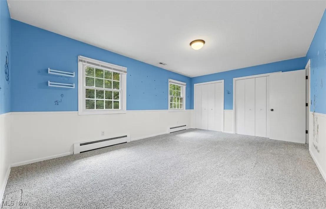 Unfurnished bedroom with multiple closets, a baseboard radiator, carpet floors, and a baseboard heating unit
