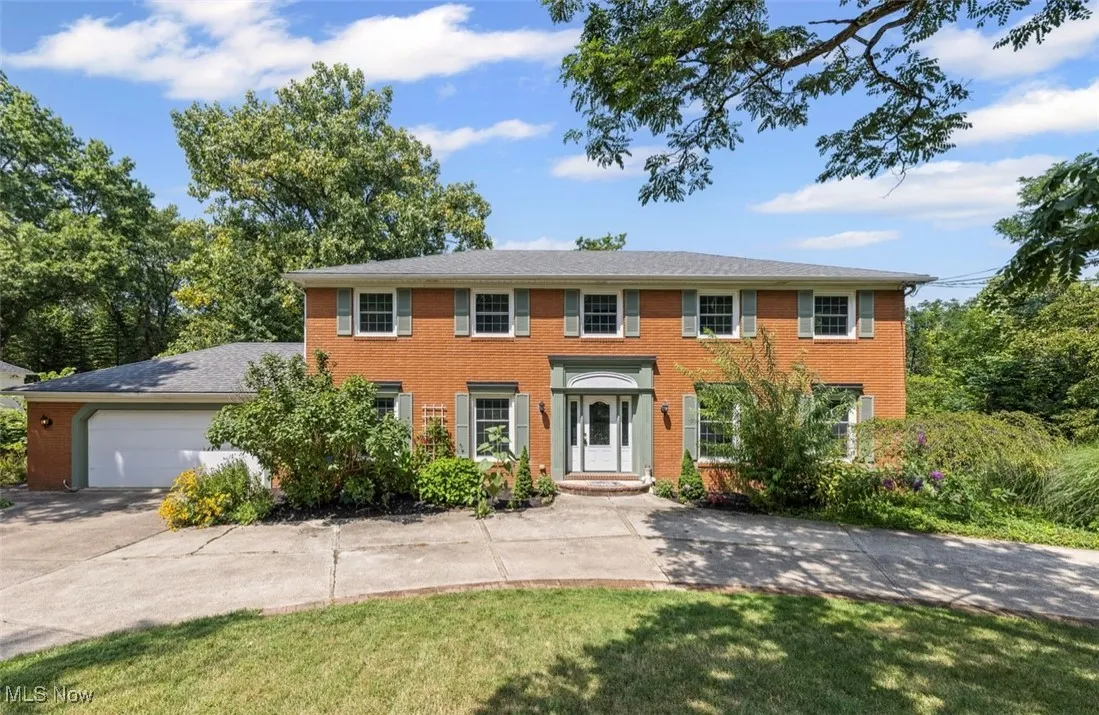 Colonial-style house with concrete driveway, brick siding, a garage, and a front yard