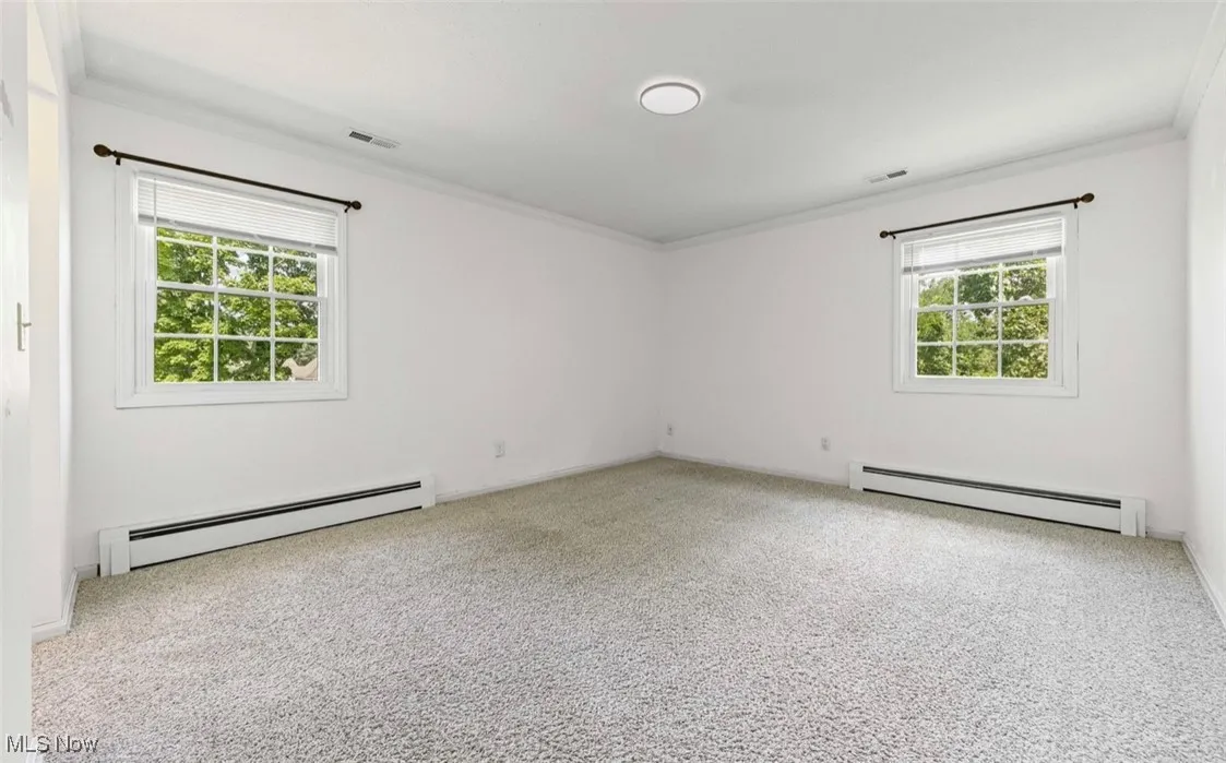 Spare room with a baseboard heating unit, crown molding, and light colored carpet