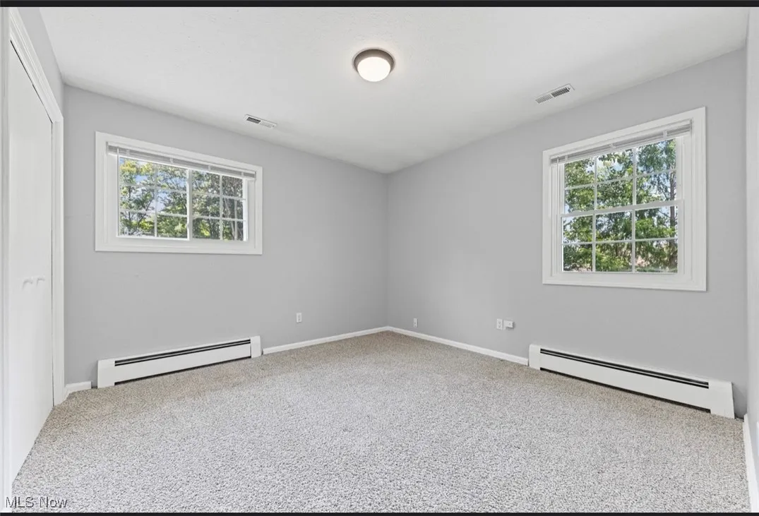 Empty room featuring baseboard heating, plenty of natural light, and carpet flooring