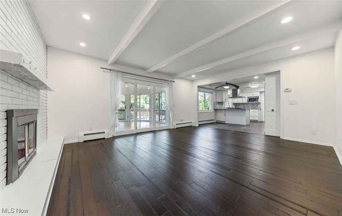 Unfurnished living room featuring beamed ceiling, a fireplace, dark wood-style floors, a baseboard radiator, and recessed lighting