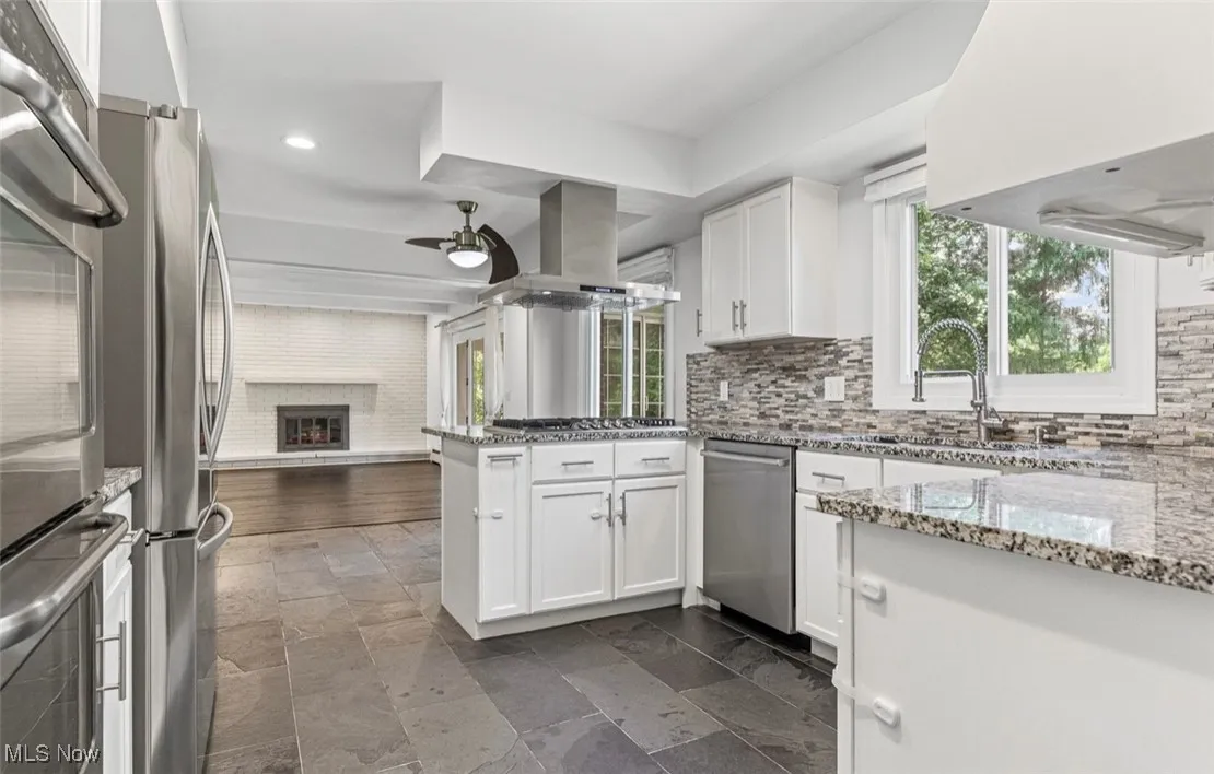 Kitchen with light stone counters, open floor plan, white cabinets, a peninsula, and backsplash