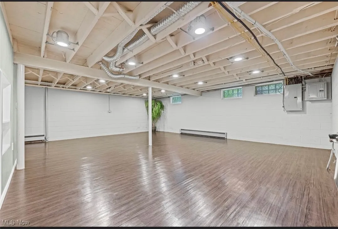 Basement featuring electric panel, wood finished floors, and a baseboard heating unit