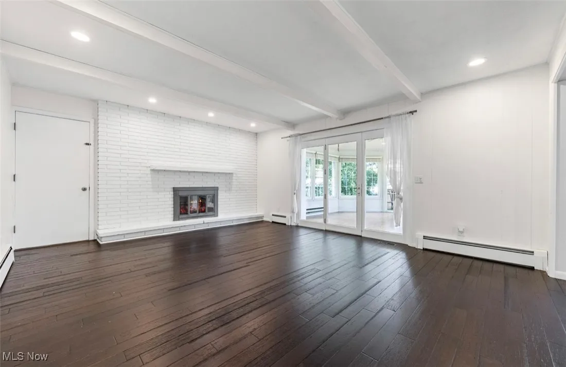 Unfurnished living room featuring beamed ceiling, baseboard heating, dark wood-type flooring, a fireplace, and recessed lighting