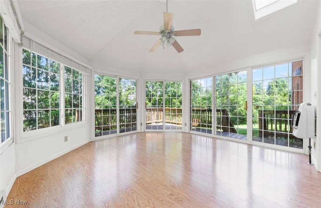 Unfurnished sunroom featuring wood finished floors, lofted ceiling, and a skylight