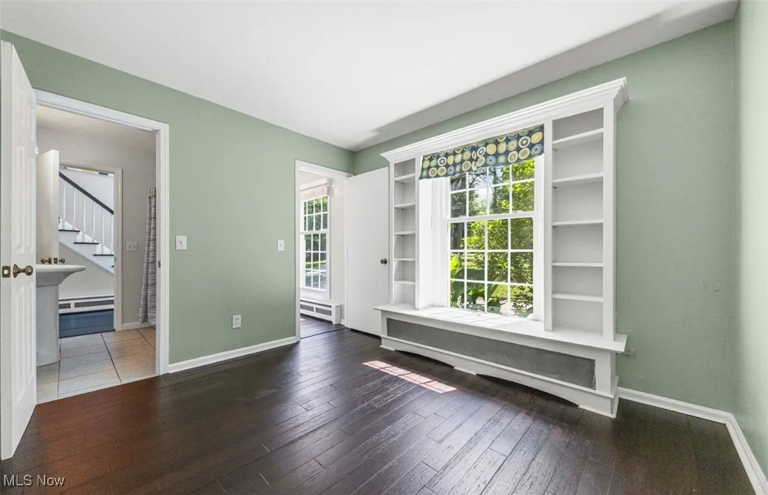 Empty room with dark wood finished floors, baseboard heating, and stairway