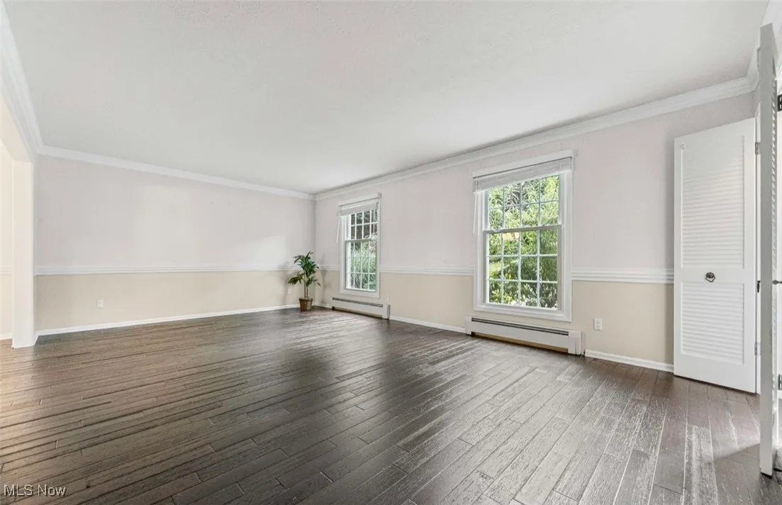 Empty room featuring ornamental molding, a baseboard heating unit, dark wood-type flooring, and a baseboard radiator