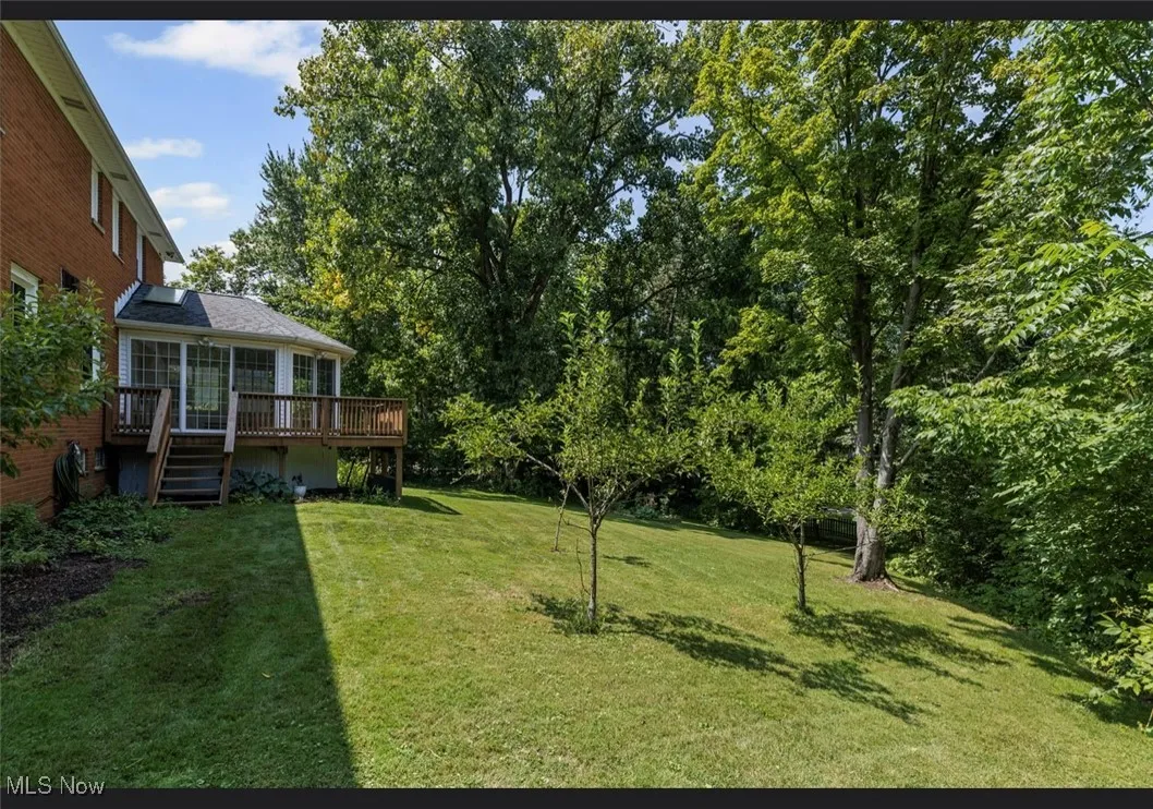 View of grassy yard featuring stairs, a wooden deck, and view of wooded area