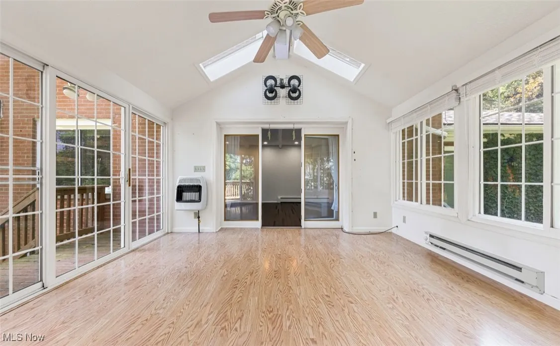 Unfurnished sunroom with a skylight, vaulted ceiling, a baseboard heating unit, wood finished floors, and healthy amount of natural light