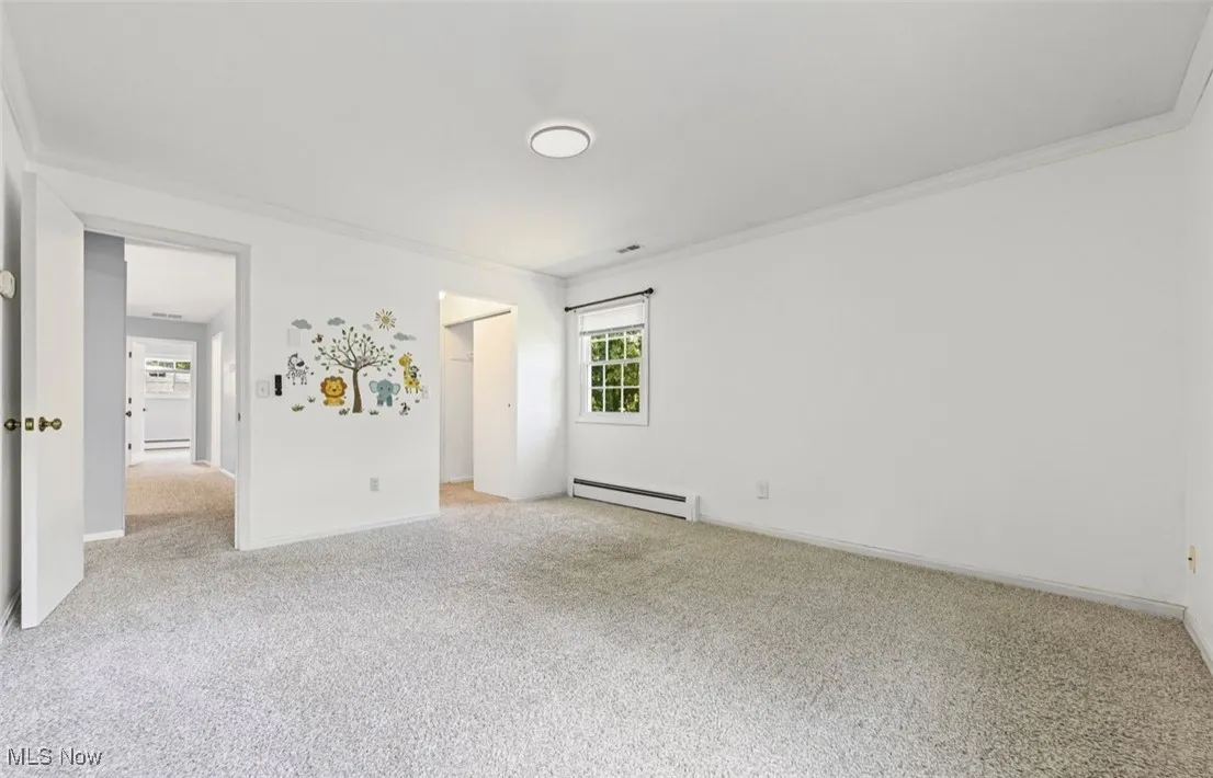Carpeted empty room featuring ornamental molding and a baseboard heating unit