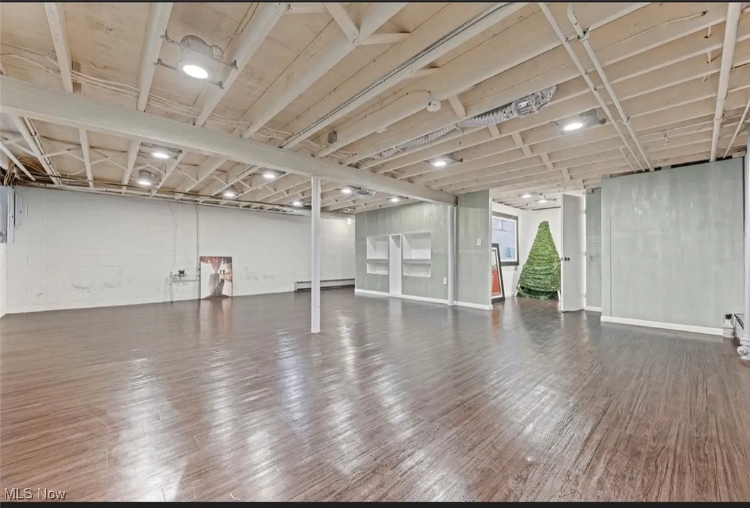 Unfinished below grade area with dark wood-type flooring, baseboard heating, and concrete block wall