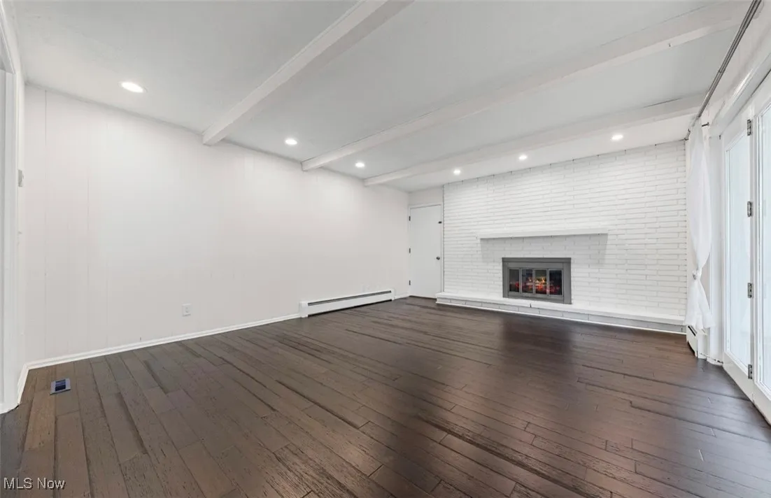 Unfurnished living room featuring beamed ceiling, dark wood finished floors, a fireplace, baseboard heating, and recessed lighting