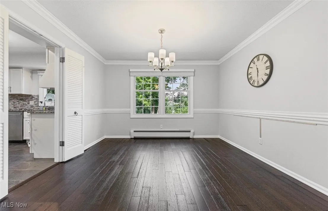 Unfurnished dining area featuring dark wood-style floors, ornamental molding, a chandelier, and a baseboard heating unit