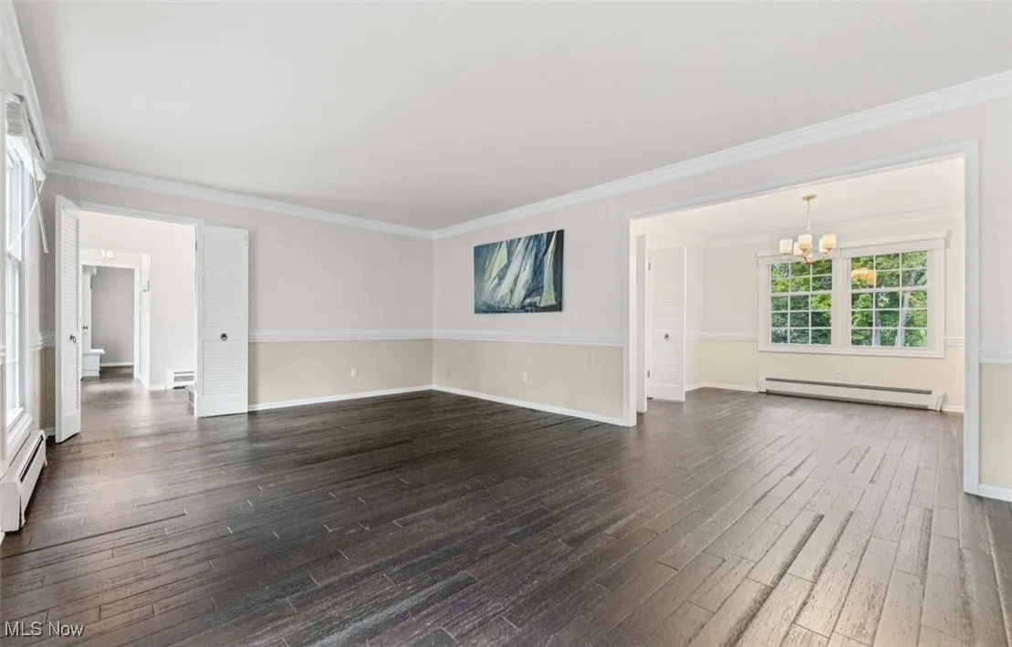 Unfurnished living room featuring crown molding, baseboard heating, a chandelier, dark wood-style floors, and a baseboard radiator