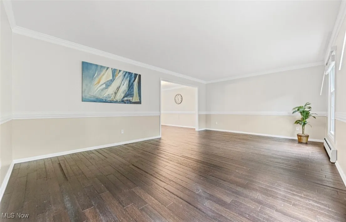 Empty room with ornamental molding, dark wood-type flooring, and a baseboard heating unit